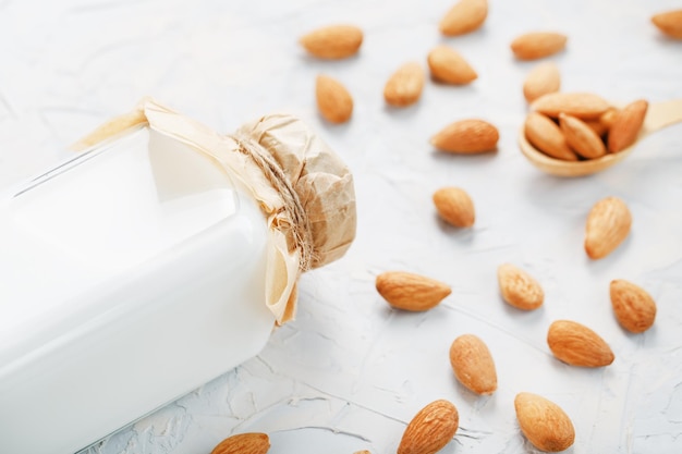 Lait d'amandes biologiques dans une bouteille transparente avec une dispersion de graines et une cuillère en bois sur fond clair