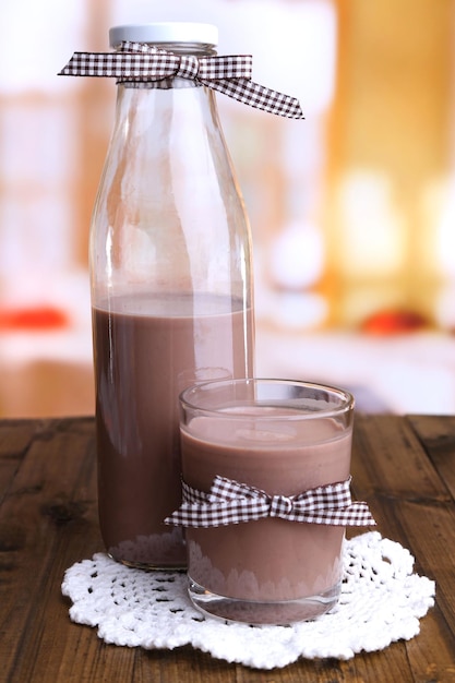 Lait au chocolat en bouteille et verre sur table en bois sur fond clair