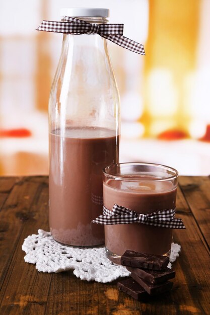 Photo le lait au chocolat dans une bouteille et un verre sur une table en bois sur un fond lumineux