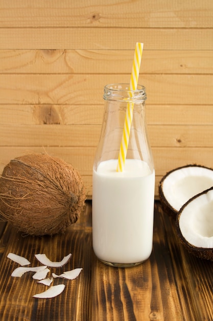 Lait de coco dans la bouteille en verre et noix de coco sur le fond en bois