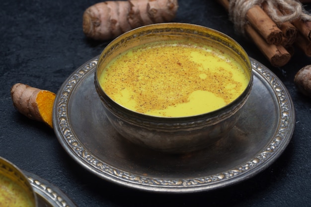 Lait de curcuma doré sur la table noire avec des ingrédients