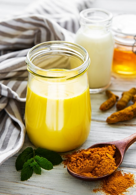 Lait doré avec cannelle, curcuma, gingembre et miel sur une surface en bois blanche