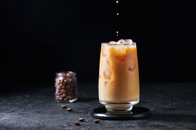 Le lait est versé dans du café glacé dans un grand verre sur fond sombre. Concept Rafraîchissant Boisson D'été.