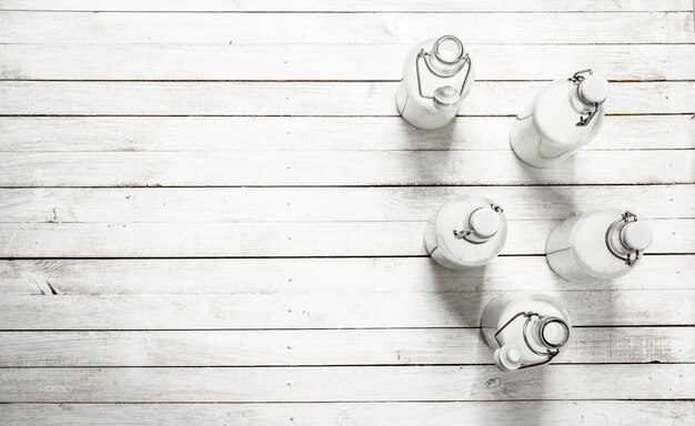 Lait frais en bouteilles sur table en bois blanc.