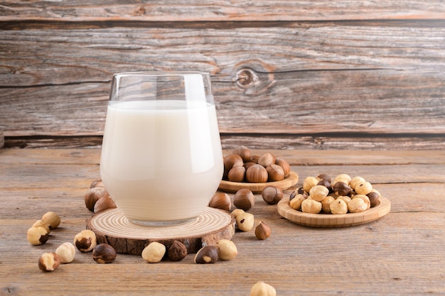 Lait de noisette végétalien non journalier en verre avec noisettes entières sur fond de bois Lait végétal alternatif