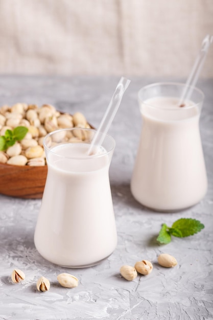 Lait de pistache biologique non laitier en verre et plaque de bois avec pistaches sur fond de béton gris. Concept d'aliments sains végétaliens, gros plan, vue latérale.