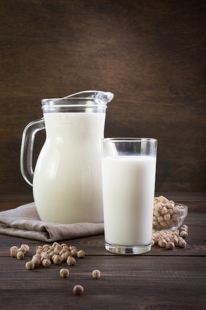 Lait de pois chiches frais en verre et pichet sur une table en bois sombre. Style rustique.