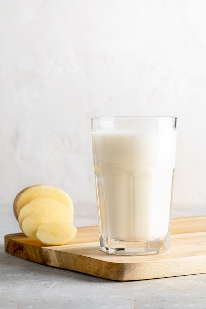 Lait de pomme de terre végétale dans un tubercule purifié de pomme de terre en verre sur une planche de cuisine en bois sur fond neutre