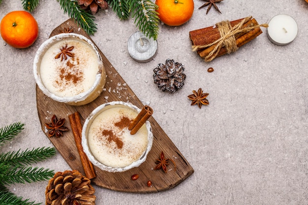 Lait de poule à la cannelle et à la muscade pour les vacances de Noël et d'hiver. Boisson maison dans des verres à bord épicé. Mandarines, bougies, cadeau.