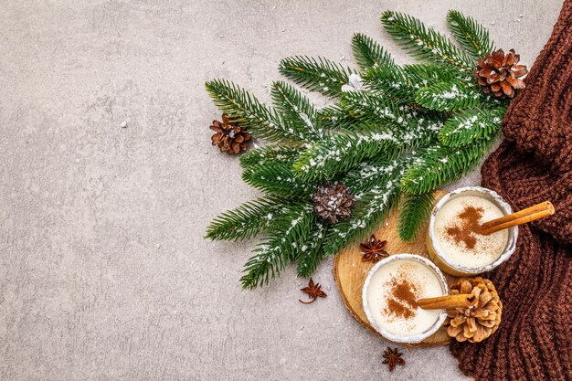 Lait de poule maison à la cannelle en verre. Dessert de Noël typique. Brunch de sapin à feuilles persistantes, cônes, plaid confortable, neige artificielle.