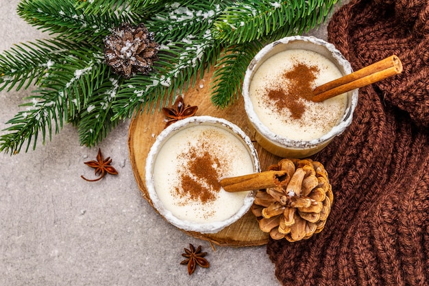 Lait de poule maison à la cannelle en verre. Dessert de Noël typique. Brunch de sapin à feuilles persistantes, cônes, plaid confortable, neige artificielle.