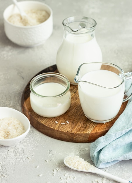 Lait de riz dans des pichets et riz dans un bol en céramique blanche et cuillère sur une pierre gris clair.