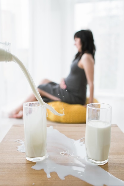 Le lait se déverse dans le verre et se renverse sur la table figure floue de la femme enceinte en arrière-plan Concept d'allaitement et de soins de santé pendant la période de la maternité