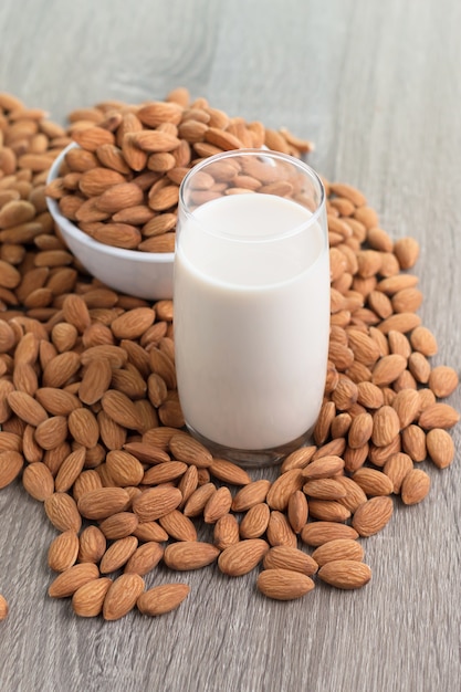 Photo lait et tas de noix d'amandes dans un bol de temps sur fond en bois