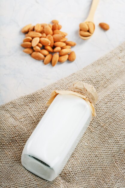 Lait végétalien à partir d'une poignée de graines d'amandes biologiques dans une bouteille sur fond clair.