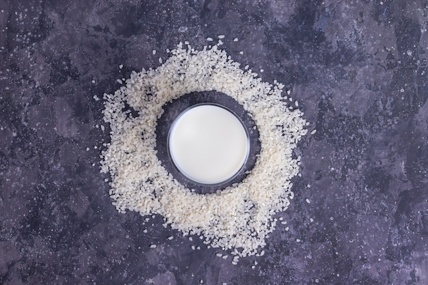 Lait végétalien de riz dans une tasse en verre avec du riz sur fond gris