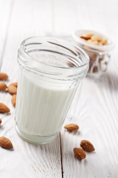 Lait ou yaourt en pot Mason sur une table en bois blanche avec des amandes dans un récipient hermétique de côté