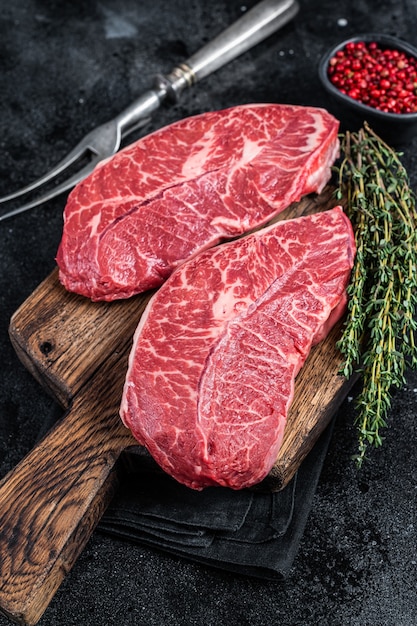 Lame supérieure crue fraîche ou steaks de viande de bœuf en fer plat sur une planche à découper de boucherie. Vue de dessus.