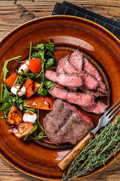 Lame supérieure d'huître rôtie au barbecue ou steak de viande de rosbif en fer plat sur une assiette avec salade. Fond en bois. Vue de dessus.