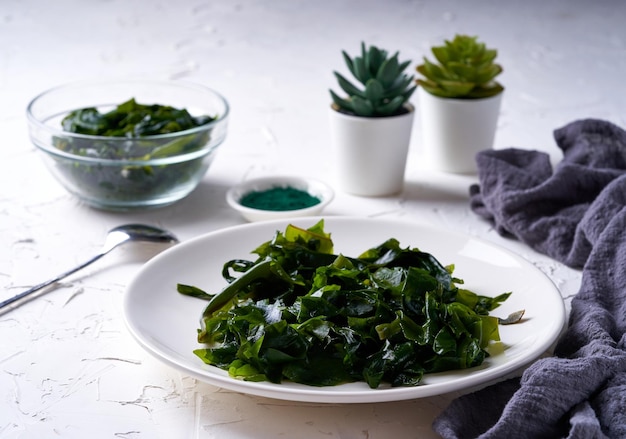 Laminaria Algue de varech et poudre de spiruline dans un bol à verres avec une cuillère en bois fond blanc