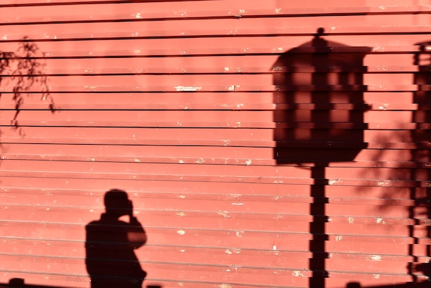 Un lampadaire et une ombre de personne sur un mur en bois rouge