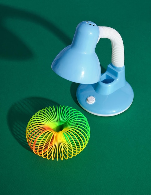 Lampe de bureau de couleur bleue sur table verte et sa lumière affichée sous forme de jouet en spirale arc-en-ciel. Composition de travail minimale.