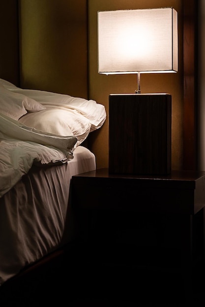 La lampe de chevet s'allume dans la chambre au crépuscule.
