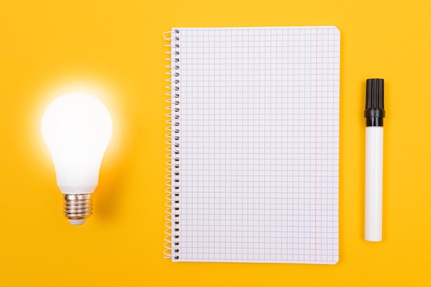 Lampe à économie d'énergie rougeoyante avec bloc-notes allongé sur une table jaune