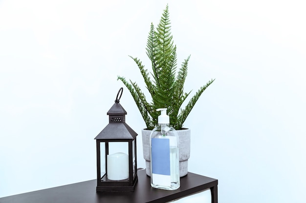 Une lampe de poche avec une bougie, une fougère verte dans un pot de fleurs et une bouteille de désinfectant à la réception du bureau.