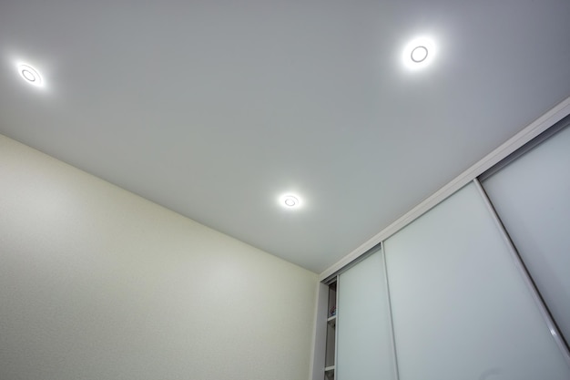 Lampes halogènes sur plafond suspendu et construction de cloisons sèches dans une pièce vide d'un appartement ou d'une maison Plafond tendu blanc et forme complexe