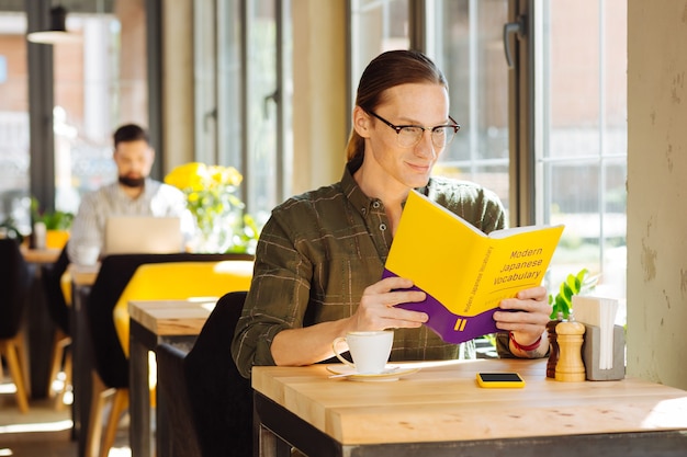 Langage difficile. Bel homme positif lisant un livre tout en étudiant le vocabulaire japonais