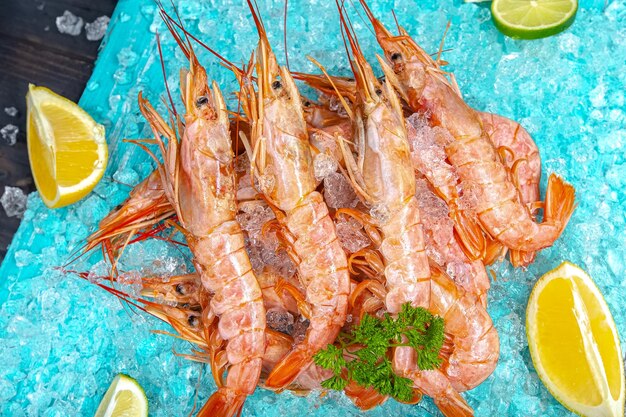 langoustines de crevettes fraîches rouges avec et sans tête, allongées sur le fond bleu glace de la mer, cerise