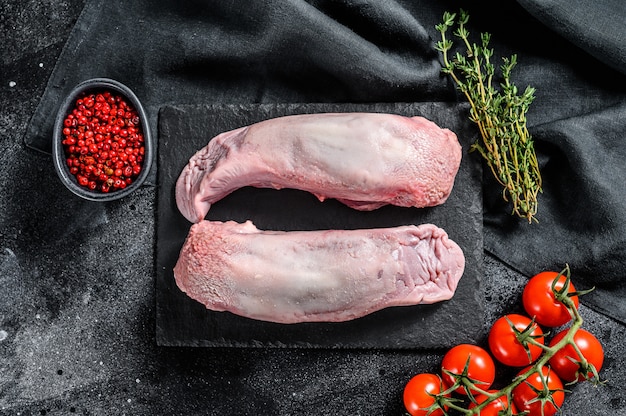 Langue de porc crue avec des épices et des herbes sur la plaque. Fond noir.