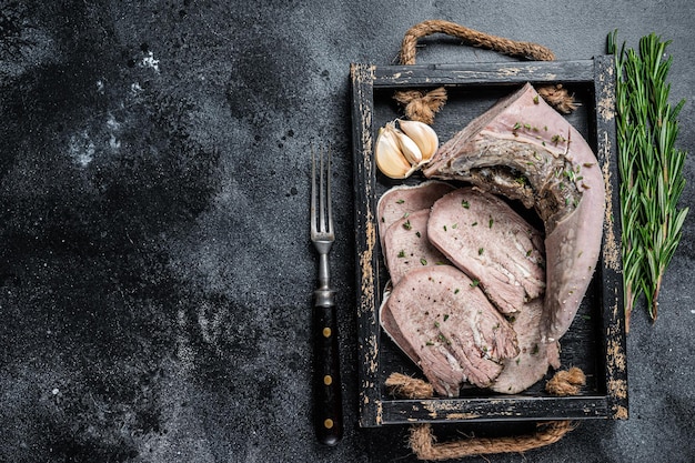 Langue de veau ou de boeuf bouillie cuite en tranches dans un plateau en bois. Fond noir. Vue de dessus. Espace de copie.