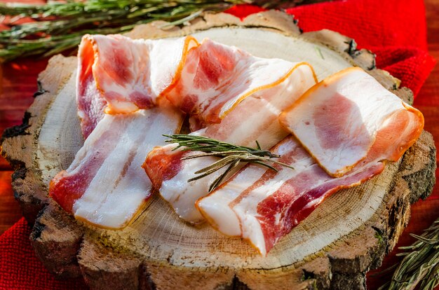 Lanières de bacon frais et d'épices sur une planche de bois