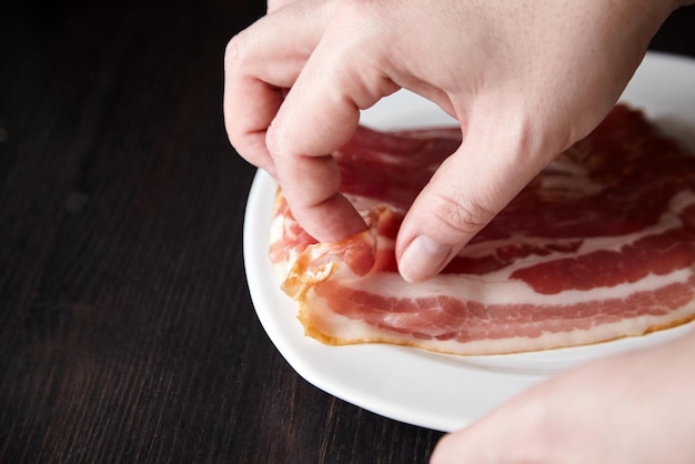 Lanières de bacon et tranches de viande de porc fumée crue de mains féminines sur une plaque blanche sur fond de tableau noir