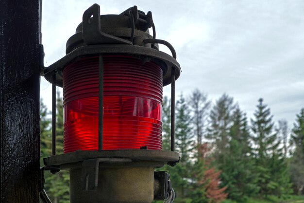 Lanterne cylindrique rouge métallisée cannelée suspendue à un poteau en bois contre des conifères flous