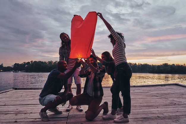 Lanterne en forme de coeur. Toute la longueur des jeunes en tenue décontractée allumant une lanterne céleste