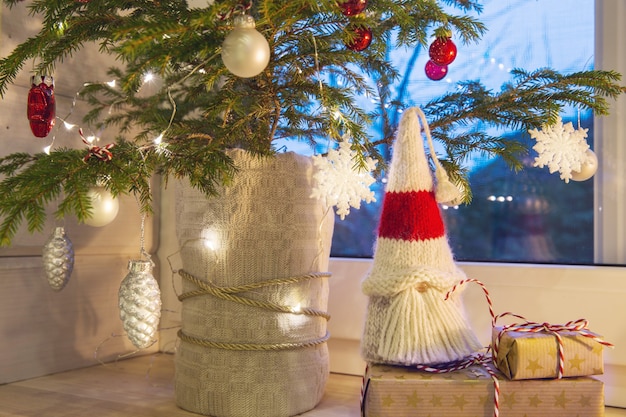 Photo lanterne de noël, gnome de noël, cadeau, arbre de noël et décor rouge sur la fenêtre d'une maison en bois donnant sur le jardin d'hiver. composition de noël