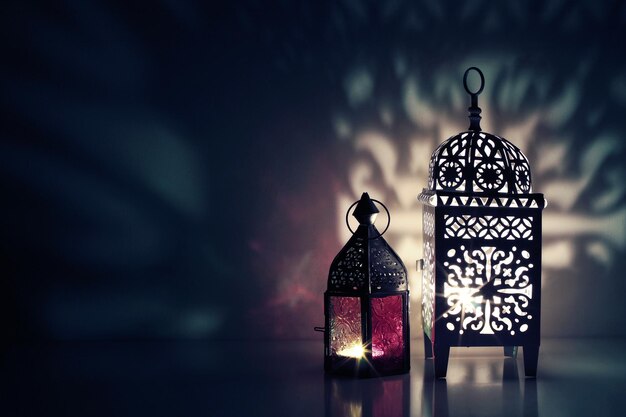 Photo lanternes ornementales marocaines sur la table qui brillent la nuit invitation de carte de voeux pour le mois sacré musulman ramadan kareem fond bleu festif avec lumière ornementale et jeux d'ombres