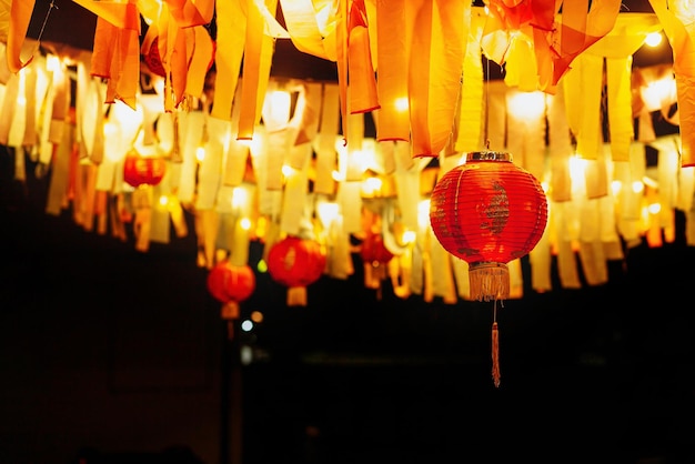 Des lanternes rouges en papier chinois pendent avec des guirlandes de rubans et des lampes la nuit dans la cour