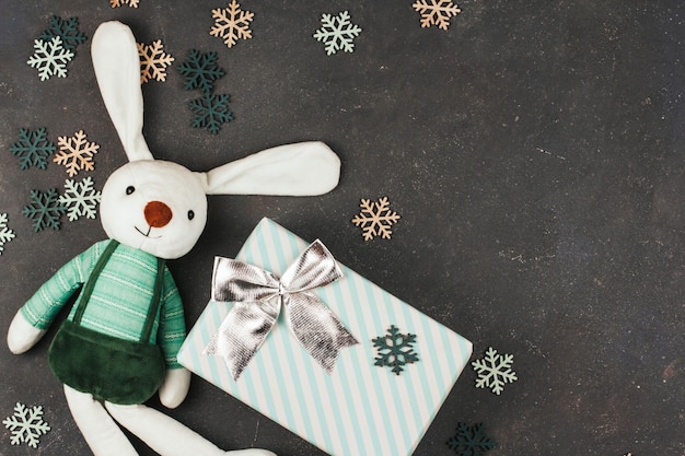 Lapin jouet blanc, coffret cadeau avec noeud et flocons de neige en bois sur fond gris foncé.