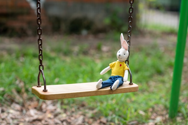 Un lapin jouet lumineux se trouve sur une balançoire en bois dans l'aire de jeux laissée par un enfant
