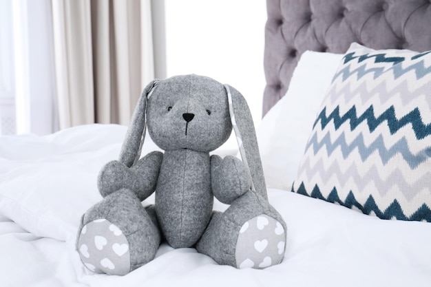 Lapin jouet mignon assis sur le lit à l'intérieur