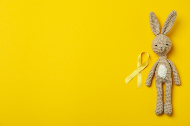 Lapin jouet et ruban de sensibilisation au cancer de l'enfant sur fond jaune