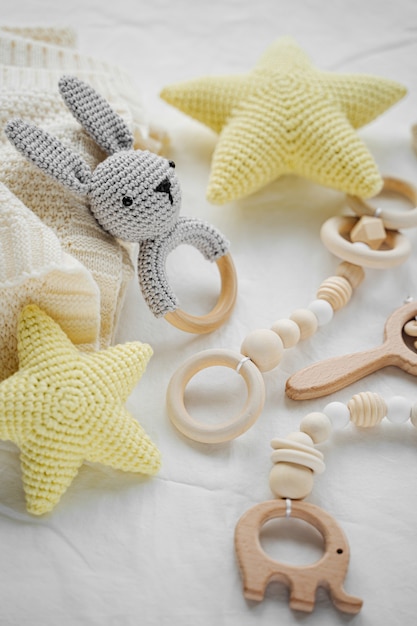 Photo lapin jouet tricoté, étoiles jaunes et anneau de dentition en bois pour nouveau-né sur lit blanc. articles et accessoires pour bébé.