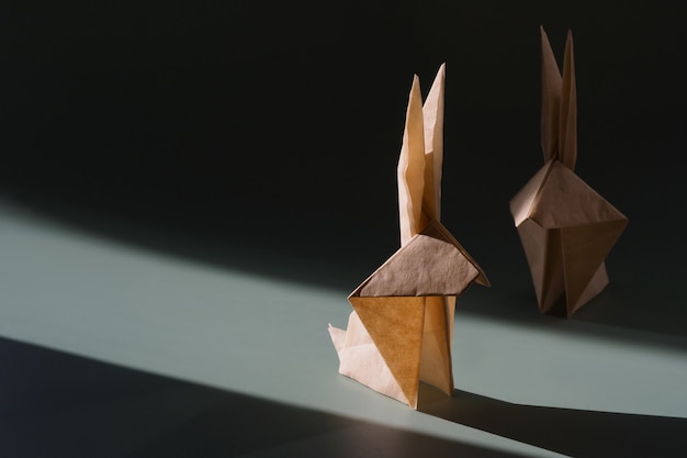 Lapin en papier origami au soleil éclatant avec des ombres dures. Artisanat en papier. Le concept minimal de Pâques ou de l'année du lapin. Le jeu d'ombre et de lumière.