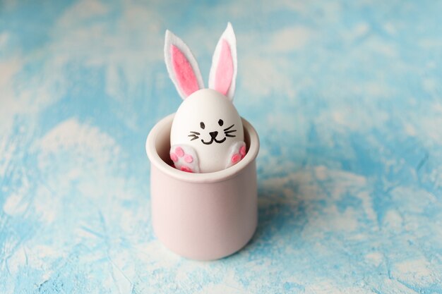 Lapin de Pâques drôle placé dans la tasse rose sur le fond bleu.