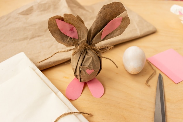 Lapin de Pâques fait d'un œuf de poule brun et de papier kraft dans les mains d'une fille, gros plan