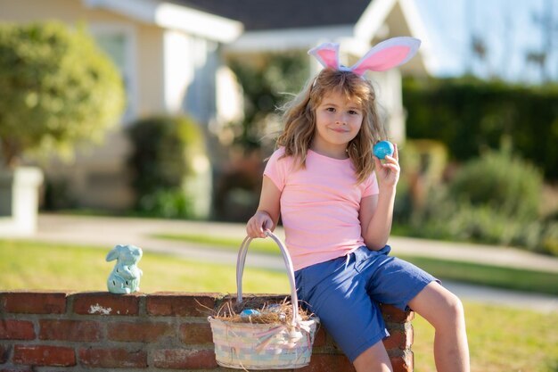 Lapin de Pâques garçon enfant dans des oreilles de lapin chassant les oeufs de pâques en plein air sur l'arrière-cour